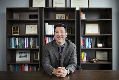 man sitting at desk with bookcase behind him