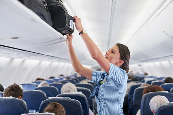 flight attendant putting luggage in overhead bin. 