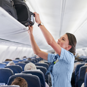 flight attendant putting luggage in overhead bin. 